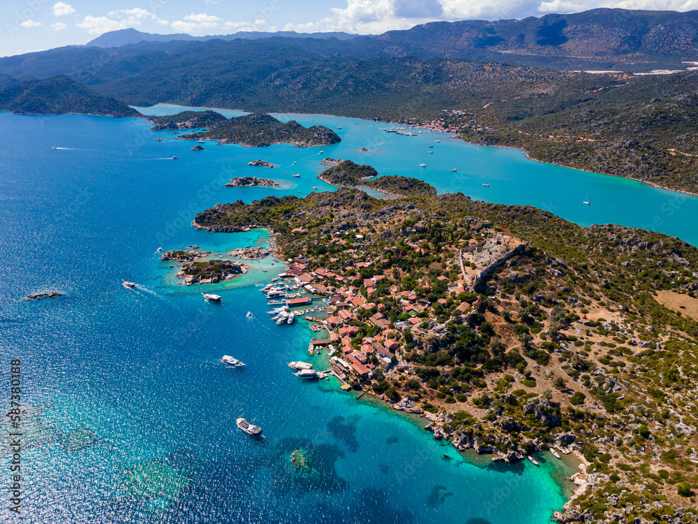 Aerial drone shot of Simena Castle (Kaleköy), beach, and yachts, displaying the historic site and enchanting Mediterranean landscape in Antalya, Turkey.