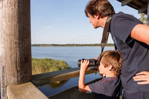 boy looking in binoculars with his father standing behind