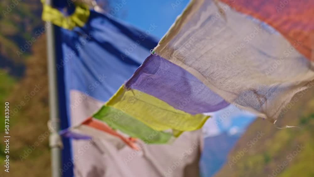Closeup of colorful Buddhist prayer flags blowing in the wind outdoors with larger flag post in the background