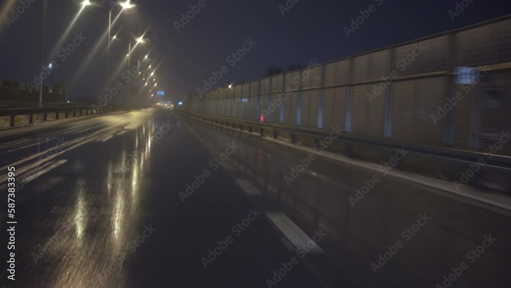 Car travels along paved route passing sound screen and lampposts