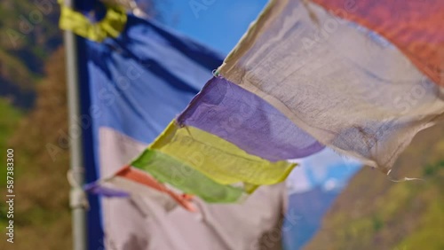 Closeup of colorful Buddhist prayer flags blowing in the wind outdoors with larger flag post in the background