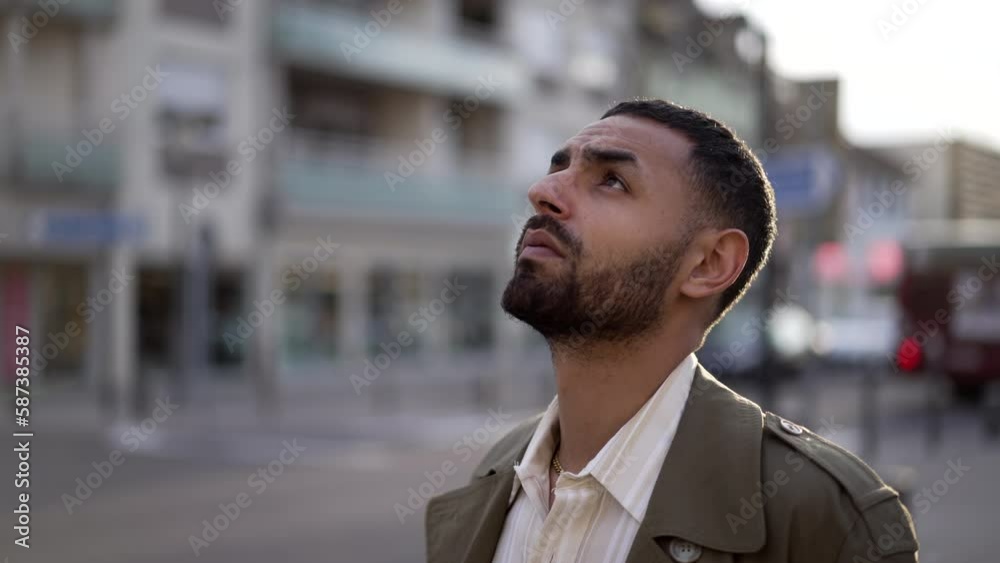 One thoughtful Middle Eastern young man standing in street looks up at sky with HOPE and FAITH. Smiling face closeup turning head upwards One thoughtful Middle Eastern young man standing in street looks up at sky with HOPE and FAITH. Smiling face closeup turning head upwards