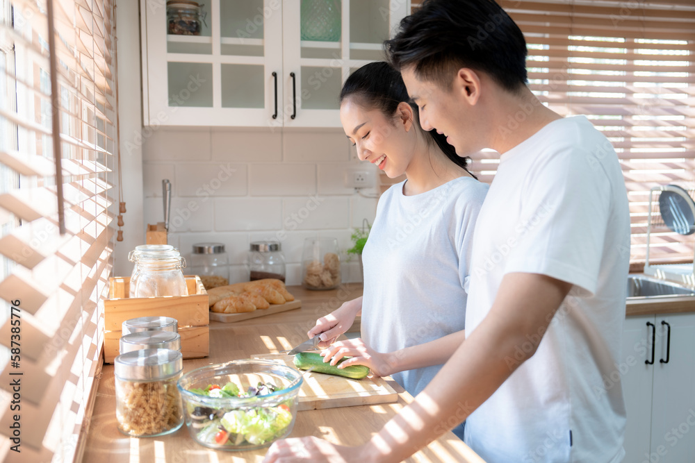 Beautiful young Asian couple is talking and smiling while cooking healthy food in kitchen at home.