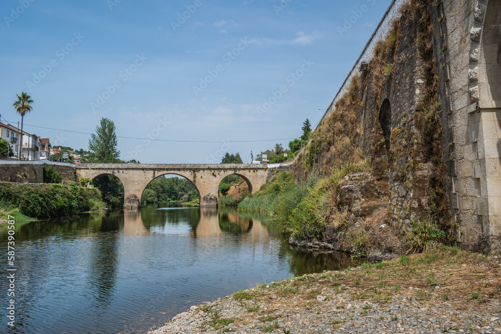 Wall of ancient stone bridge with herbs and medieval bridge of Coja in the background reflected in the river Alva, Arganil PORTUGAL