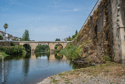 Wall of ancient stone bridge with herbs and medieval bridge of Coja in the background reflected in the river Alva, Arganil PORTUGAL photo