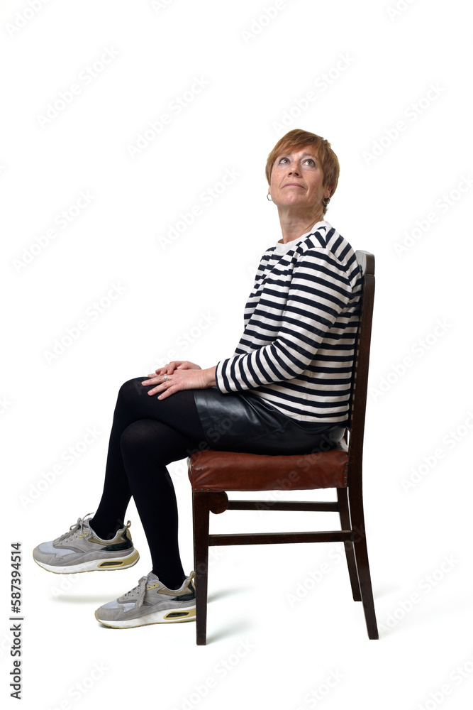 side view full length portrait of a woman in skirt, striped sweater and sneakers sitting on chair and legs crossed looking up on white background side view full length portrait of a woman in skirt, striped sweater and sneakers sitting on chair and legs crossed looking up on white background
