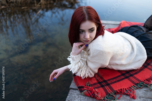 Relaxed Redhaired girl in sweater lying on a pier by natureal lake in autumn. photo