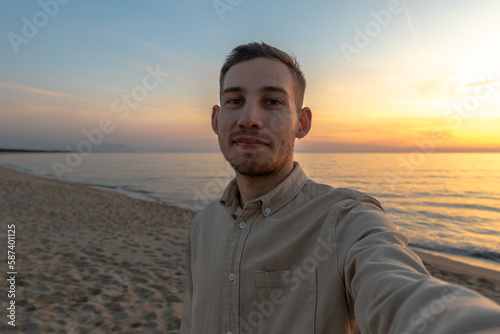 young man in a shirt, taking a selfie in a sunset on the beach