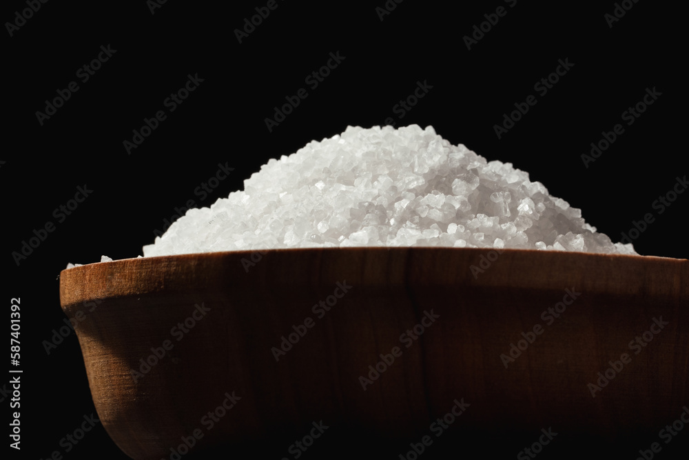 Coarse white salt in a wooden bowl on the black background Coarse white salt in a wooden bowl on the black background