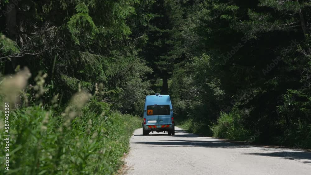 Blue van driving on evergreen forest mountain road while traveling on summer vacation, slow motion cinematic shot