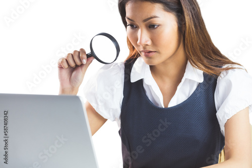 Businesswoman looking through magnifying glass and using laptop