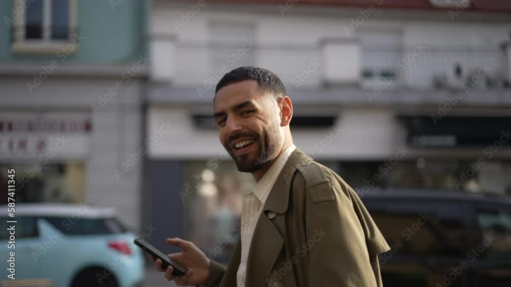 Profile face close up of a happy Arab man turning head to camera smiling while holding phone and scrolling through city streets Profile face close up of a happy Arab man turning head to camera smiling while holding phone and scrolling through city streets