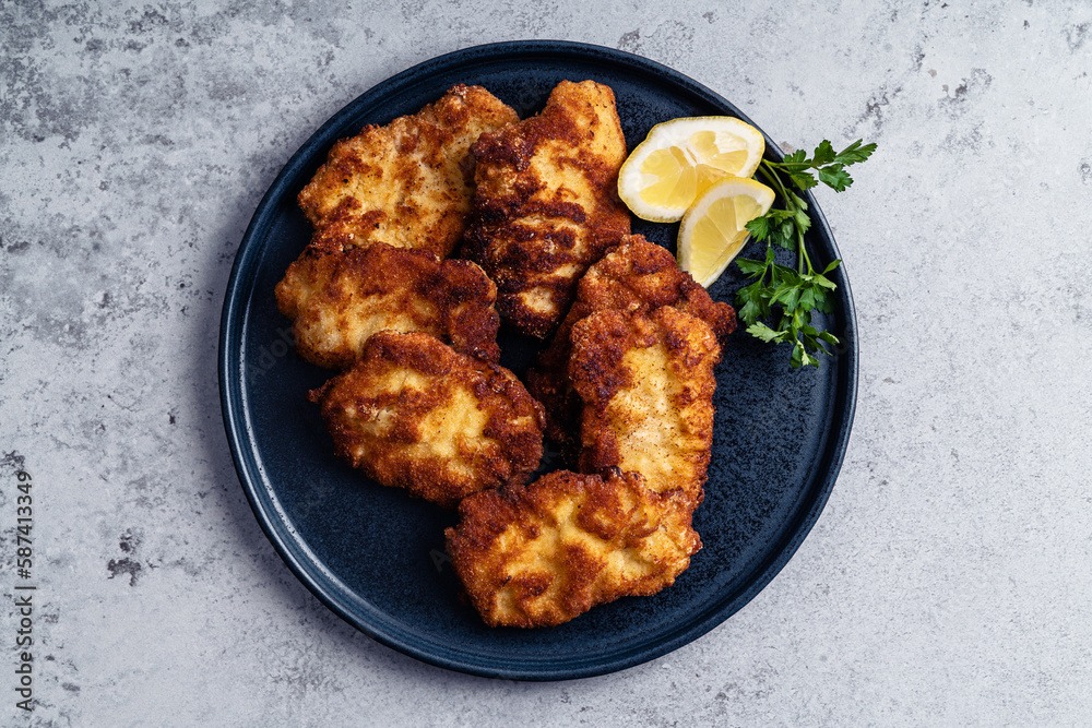 Schnitzel with slice of lemon on black plate on grey background Schnitzel with slice of lemon on black plate on grey background
