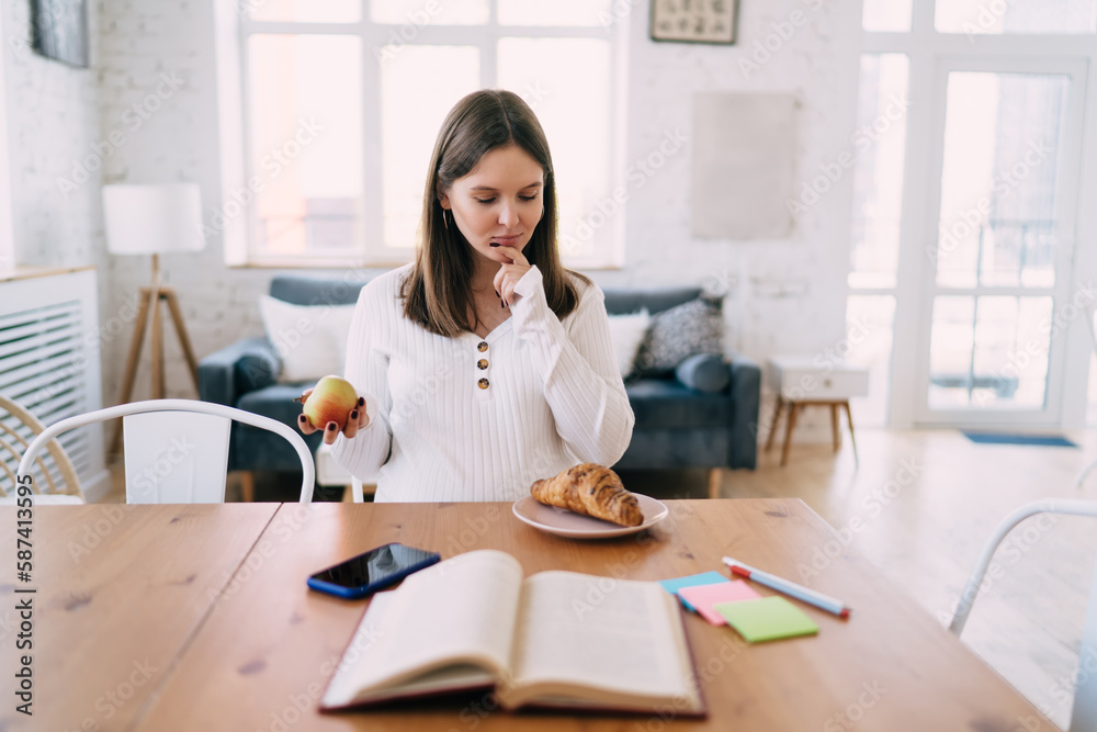 Young expectant woman sitting at table choosing snack in kitchen Young expectant woman sitting at table choosing snack in kitchen