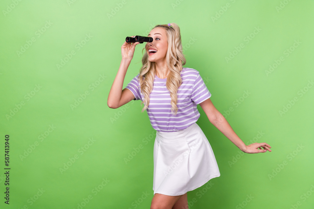 Portrait of satisfied impressed woman wavy hairstyle tabby t-shirt holding binoculars look empty space isolated on green color background Portrait of satisfied impressed woman wavy hairstyle tabby t-shirt holding binoculars look empty space isolated on green color background