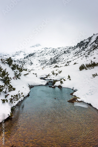 Narrow and shallow Bunderishka river between Ribno lake and Vihren hut in snowy cloudy day. Winter mountain landscape in Pirin national park, Bulgaria. photo