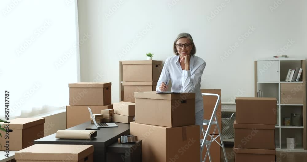 Confident mature woman retail seller, individual entrepreneur smile looks at camera, pose in dropshipping storage, boxes prepared for shipment nearby. Delivery services, small business owner portrait Confident mature woman retail seller, individual entrepreneur smile looks at camera, pose in dropshipping storage, boxes prepared for shipment nearby. Delivery services, small business owner portrait