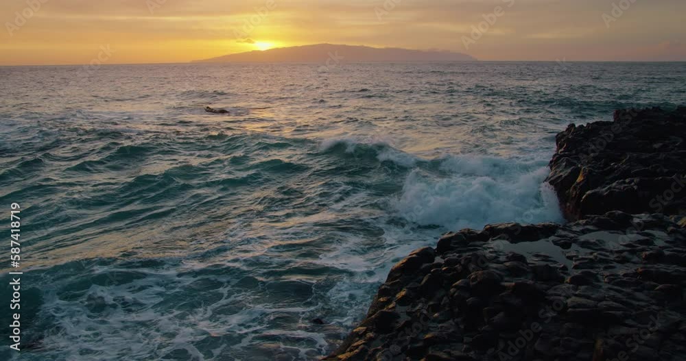 Ocean waves crash on rocks during a beautiful colourful sunset in slow-motion. Sea water spalsh spray against orange dusk sky. Ocean waves crash on rocks during a beautiful colourful sunset in slow-motion. Sea water spalsh spray against orange dusk sky.