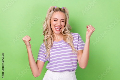 Photo of positive lucky girl wear violet t-shirt screaming shouting rising fists isolated green color background