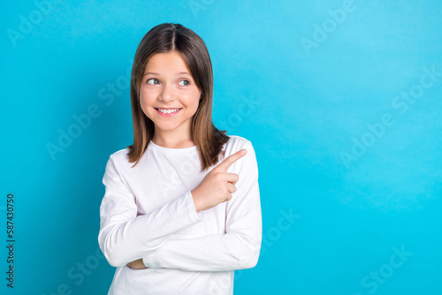 Photo portrait of cute little girl finger point look interested empty space dressed stylish white clothes isolated on blue color background