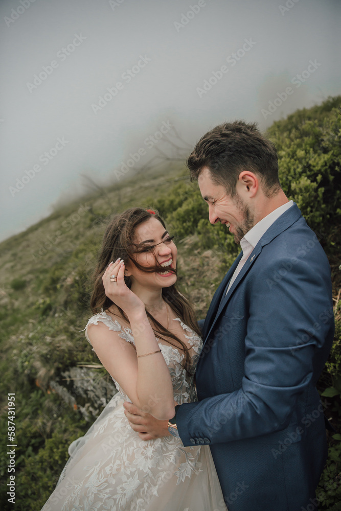 Happy wedding couple in the mountains. The bride with her long hair blowing in the wind smiles sincerely. Wedding photo session in nature. Photo session in the forest of the bride and groom.