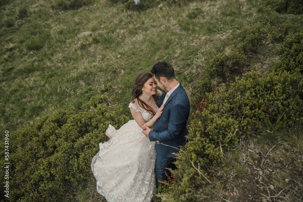 Happy wedding couple in the mountains. The bride with her long hair blowing in the wind smiles sincerely. Wedding photo session in nature. Photo session in the forest of the bride and groom.