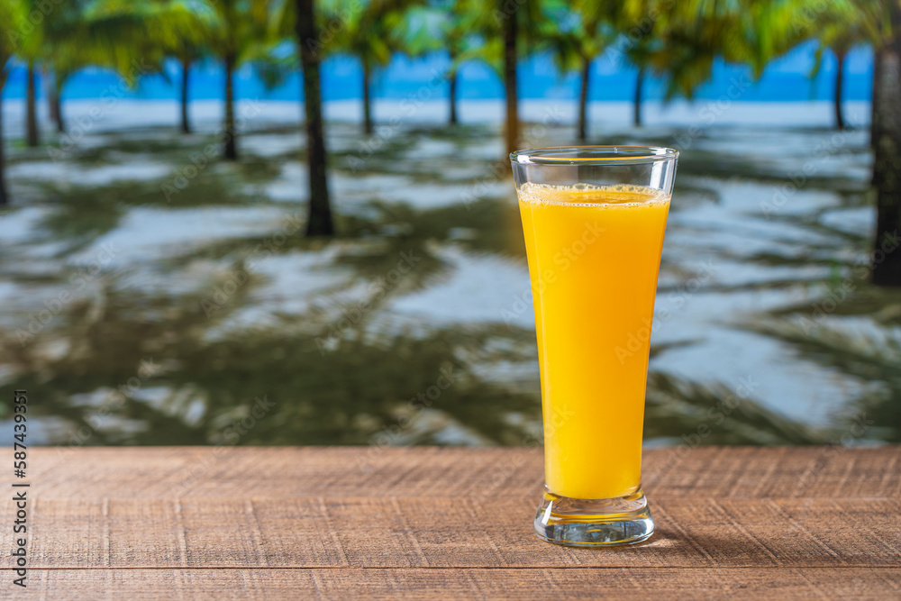 Freshly squeezed orange juice in glass on wooden table near sea on sunny summer day in tropical beach cafe, close up, copy space. Glass of fresh fruit orange juice Freshly squeezed orange juice in glass on wooden table near sea on sunny summer day in tropical beach cafe, close up, copy space. Glass of fresh fruit orange juice
