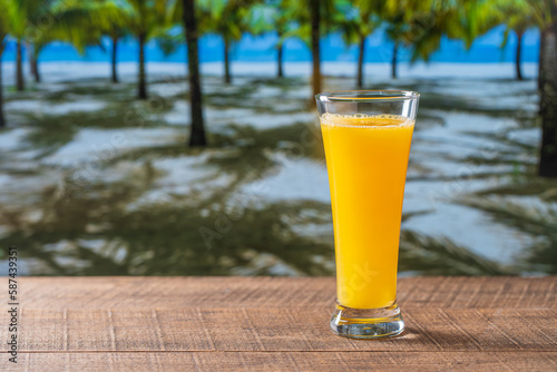 Freshly squeezed orange juice in glass on wooden table near sea on sunny summer day in tropical beach cafe  close up  copy space. Glass of fresh fruit orange juice