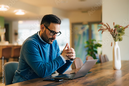 Focused businessman working over the laptop, sitting at the workplace, with glasses on. photo