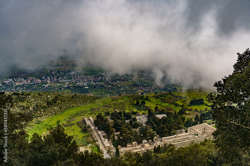 A beautiful view from above, just below the cloud line, on a hillside covered with dense foliage and the town below.