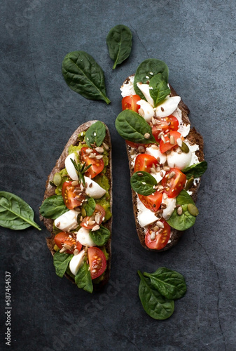 Bruschetta (sandwiches) with cherry tomatoes, mozzarella cheese and herbs on a dark background. A traditional Italian snack.
