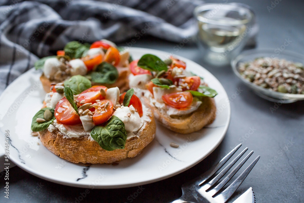 Bruschetta (sandwiches) with cherry tomatoes, mozzarella cheese and herbs on a stylish plate on a dark background. A traditional Italian snack.