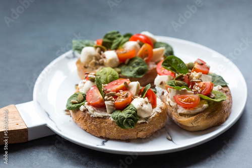 Bruschetta (sandwiches) with cherry tomatoes, mozzarella cheese and herbs on a stylish plate on a dark background. A traditional Italian snack.
