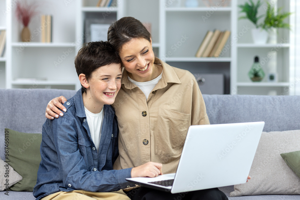 Mother and son hugging together sitting on sofa at home in living room watching video online using laptop, family spending time together watching online educational course. Mother and son hugging together sitting on sofa at home in living room watching video online using laptop, family spending time together watching online educational course.