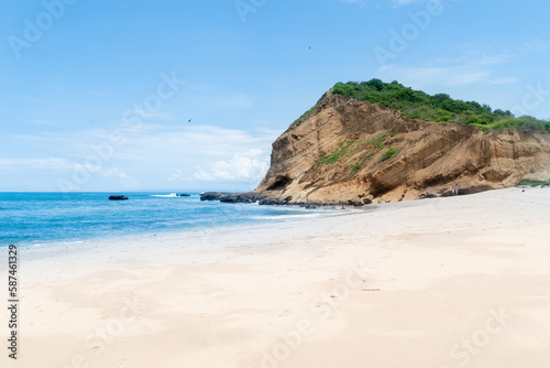 clam and flat beach of hard packed soft white powdery sand with an exposed rocky cliff that has been weathered and eroded in the distance forming a sheltered bay © _ _