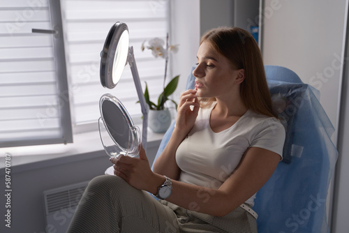 Obraz na płótnie Young beautiful woman customer with mirror getting ready for beauty procedures in a medical salon w salonie