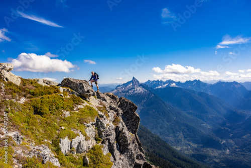 Adventurous athletic male hiker climbing up a mountain in the Pacific Northwest with jagged mountains in the background. 