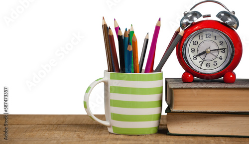 Books with alarm clock by colored pencils in mug on table