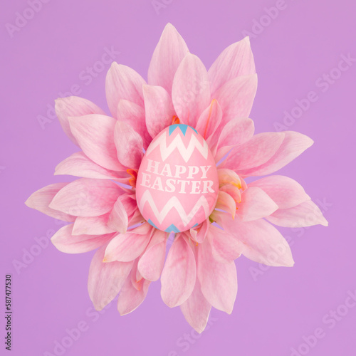 Tiny pink decorated Easter egg sitting in blooming flower with Happy Easter greeting.