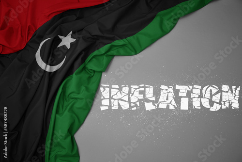 waving colorful national flag of libya on a gray background with broken text inflation. 3d illustration