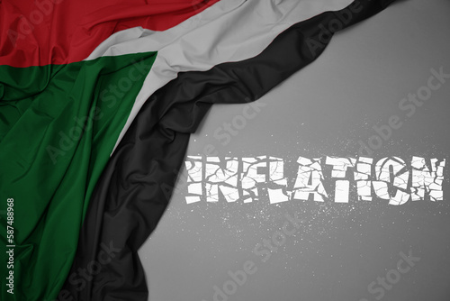 waving colorful national flag of sudan on a gray background with broken text inflation. 3d illustration
