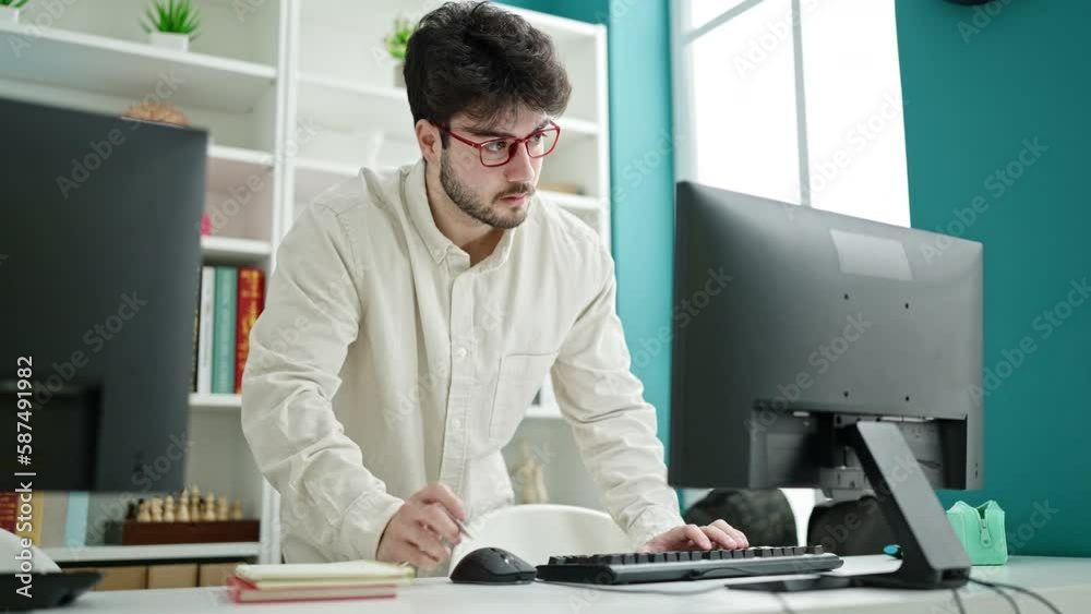 Young hispanic man student using computer writing notes at library university
