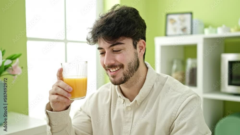 Young hispanic man holding glass of orange juice at dinning room Young hispanic man holding glass of orange juice at dinning room
