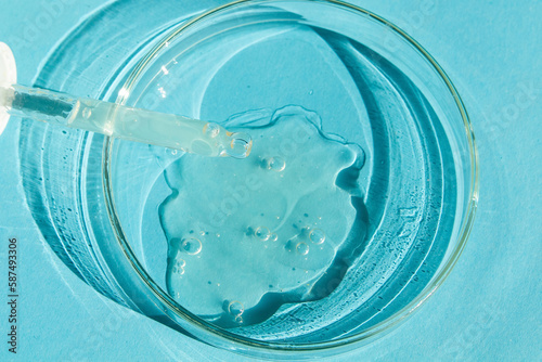 Petri dish. With transparent gel. The pipette lies. Cosmetic dispenser. On a blue background.