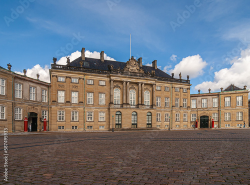 Copenhagen, Denmark - September 13, 2010: King Christian 8 brown stone palace with black roof at Amalienborg square under blue sky. Statues, pillars and windows. Red guard stations add color