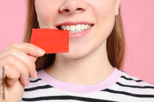 Woman holding condom on pink background, closeup. Safe sex