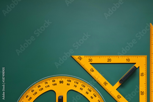Protractor and triangles on green chalkboard, flat lay. Space for text