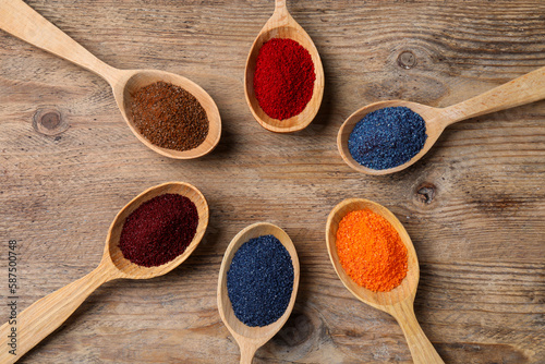 Many spoons with food coloring on wooden table, flat lay