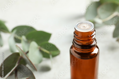 Bottle of eucalyptus essential oil and leaves on white table, closeup. Space for text