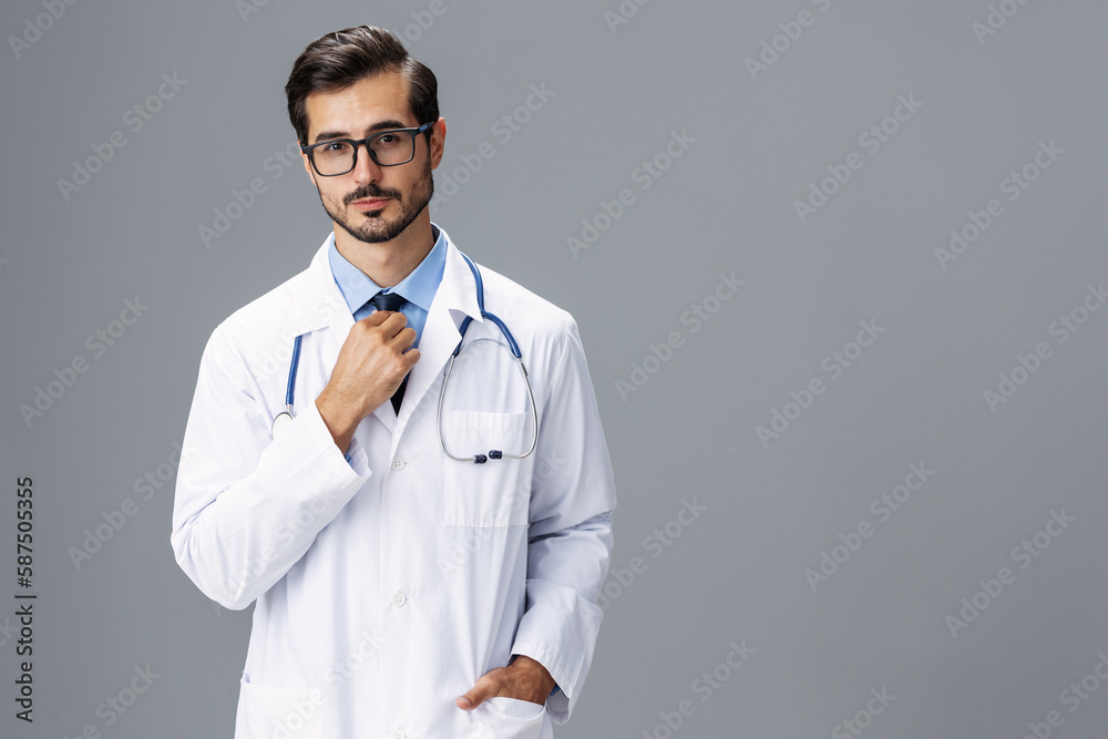 A serious doctor man in a white coat and eyeglasses and a stethoscope looks at the camera on a gray isolated background, copy space, space for text, health A serious doctor man in a white coat and eyeglasses and a stethoscope looks at the camera on a gray isolated background, copy space, space for text, health